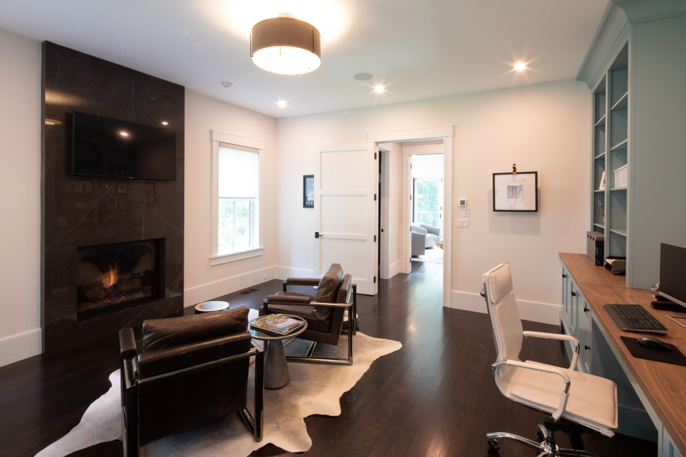 Großes Landhaus Arbeitszimmer mit weißer Wandfarbe, dunklem Holzboden, Kamin, Kaminumrandung aus Stein, Einbau-Schreibtisch und schwarzem Boden in Boston