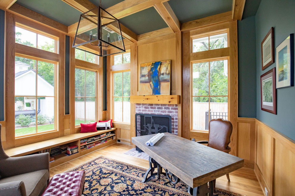 Diseño de despacho de estilo de casa de campo grande con biblioteca, paredes azules, suelo de madera clara, todas las chimeneas, marco de chimenea de ladrillo, escritorio independiente y suelo beige