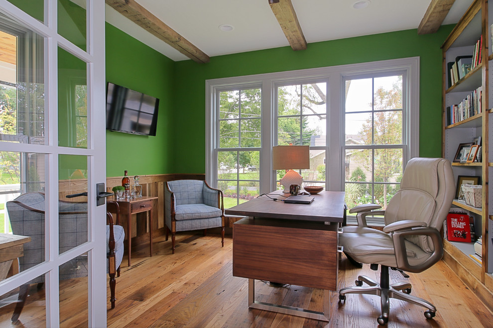 Inredning av ett lantligt stort hemmabibliotek, med gröna väggar, mellanmörkt trägolv och ett fristående skrivbord