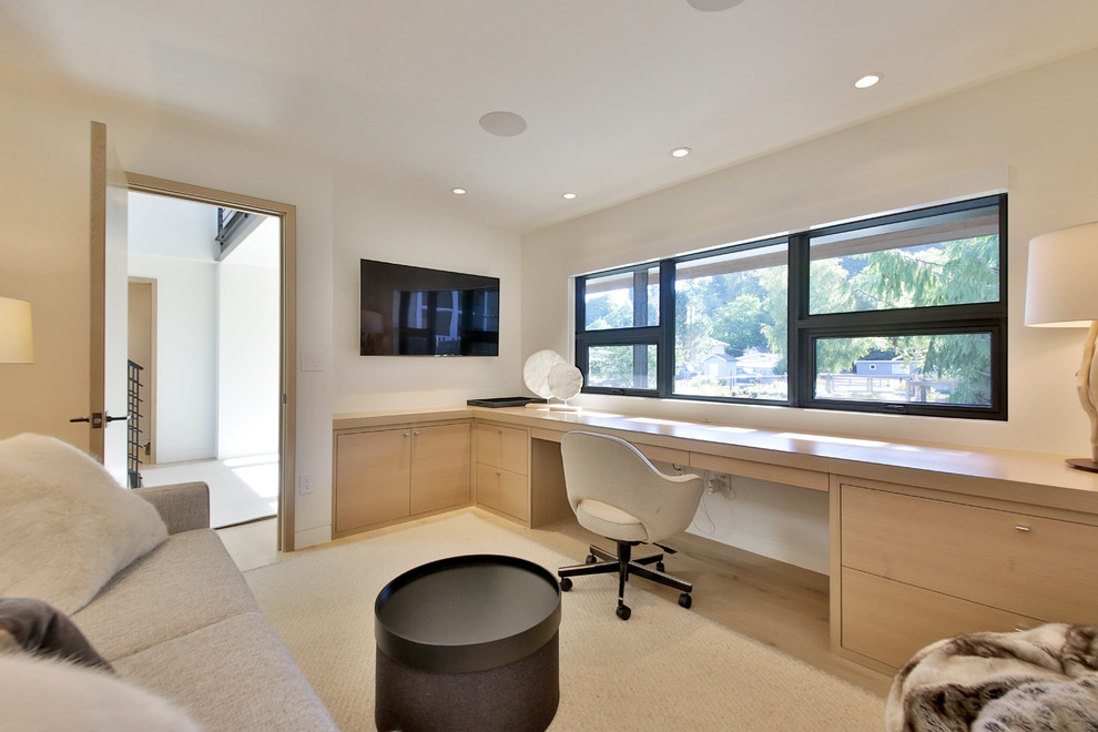 Modelo de despacho moderno de tamaño medio sin chimenea con paredes blancas, suelo de madera clara, escritorio empotrado y suelo beige