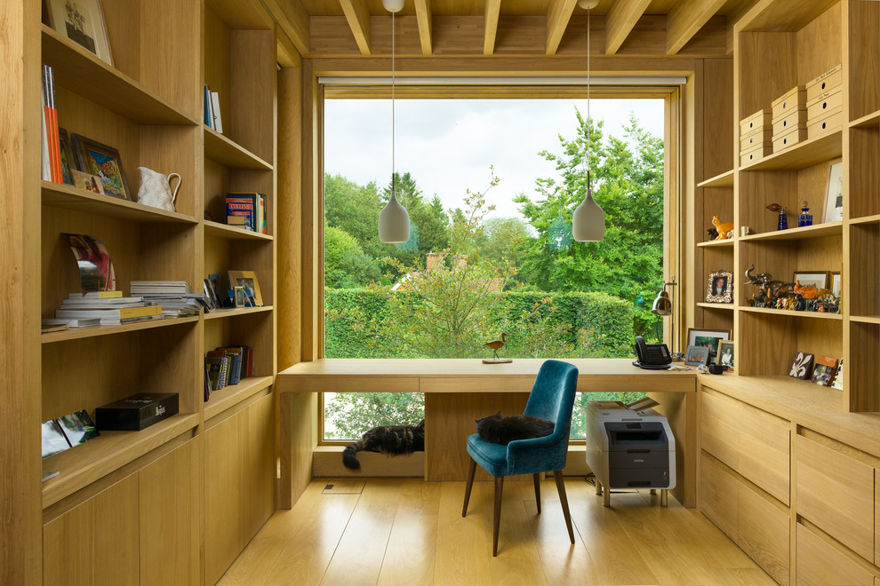 Modern inredning av ett mellanstort hemmabibliotek, med ljust trägolv, ett fristående skrivbord och beiget golv