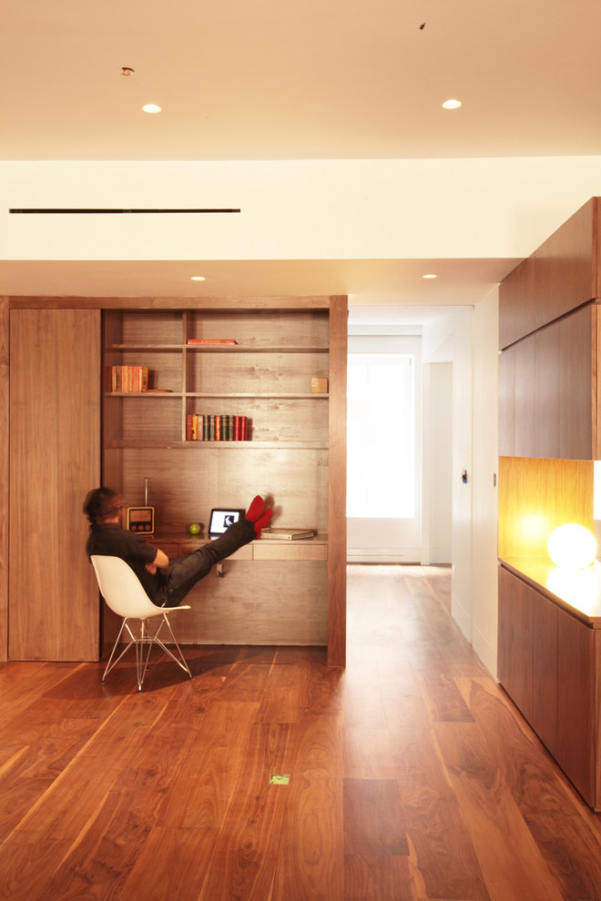 Diseño de despacho minimalista con paredes blancas, suelo de madera oscura y escritorio empotrado