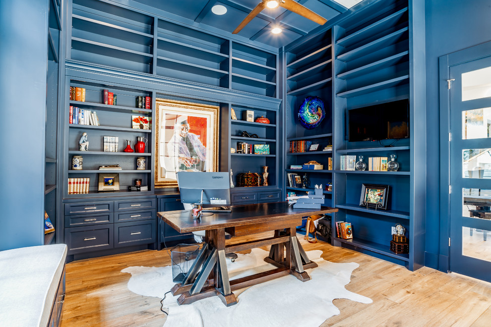 Exempel på ett stort klassiskt hemmabibliotek, med blå väggar, ljust trägolv, ett fristående skrivbord och brunt golv