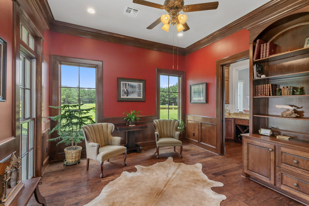 Mittelgroßes Klassisches Arbeitszimmer mit Arbeitsplatz, roter Wandfarbe, braunem Holzboden, freistehendem Schreibtisch und braunem Boden in Sonstige