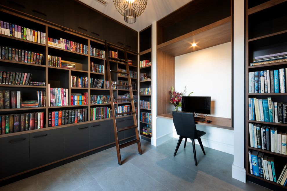 Ejemplo de despacho actual con biblioteca, paredes blancas, escritorio empotrado y suelo gris