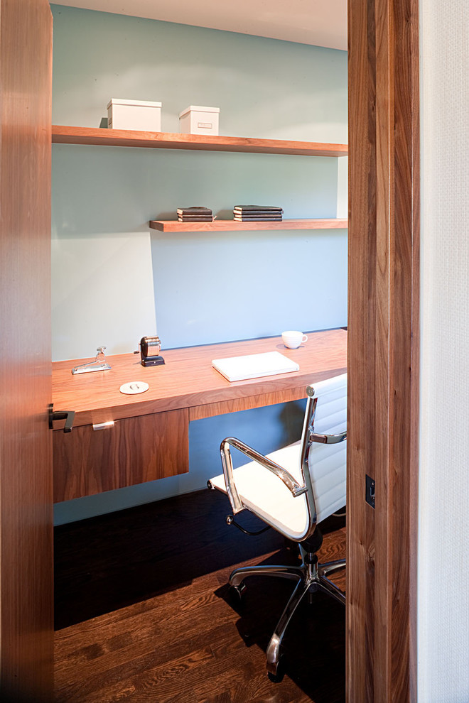 Ejemplo de despacho minimalista con paredes azules, suelo de madera oscura y escritorio empotrado