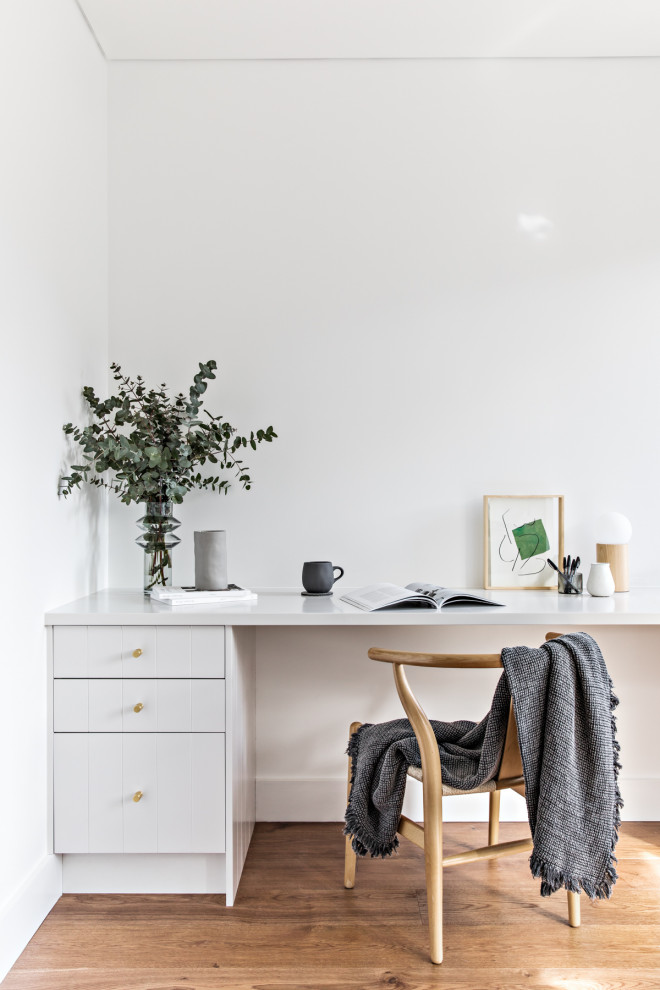 Minimalistisk inredning av ett arbetsrum, med vita väggar, mellanmörkt trägolv, ett inbyggt skrivbord och brunt golv