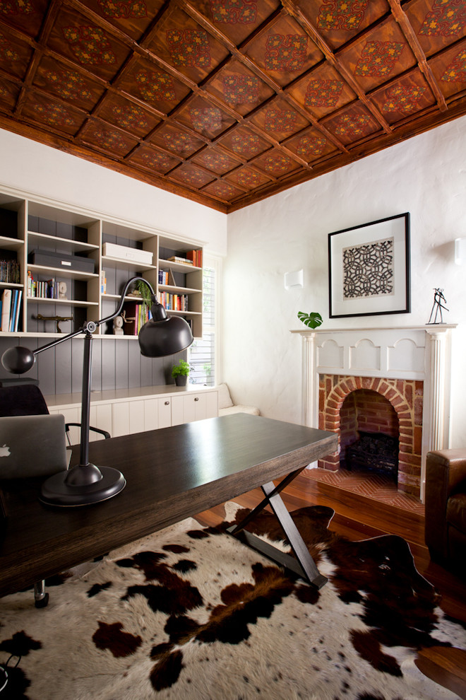 Exempel på ett mellanstort rustikt hemmabibliotek, med beige väggar, mellanmörkt trägolv, en standard öppen spis, en spiselkrans i tegelsten och ett fristående skrivbord