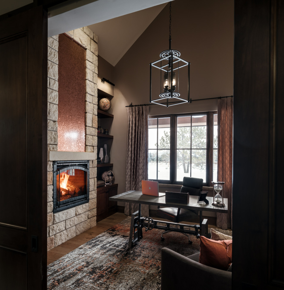 デンバーにある高級な中くらいなラスティックスタイルのおしゃれな書斎 (茶色い壁、無垢フローリング、標準型暖炉、石材の暖炉まわり、自立型机、三角天井) の写真