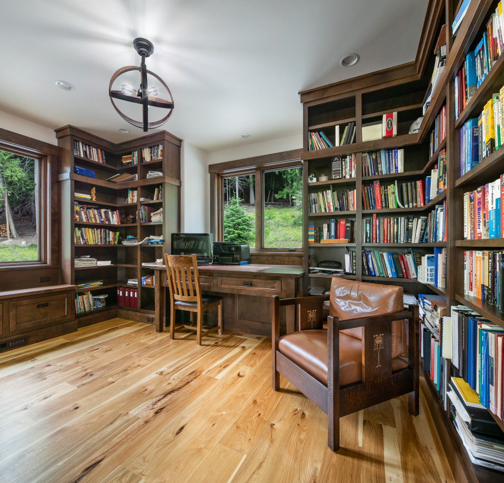 Imagen de despacho de tamaño medio con biblioteca, paredes blancas, suelo de madera en tonos medios y escritorio empotrado
