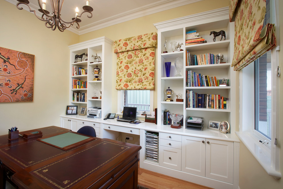 Idee per un ufficio classico con pareti gialle, pavimento in legno massello medio, nessun camino e scrivania incassata