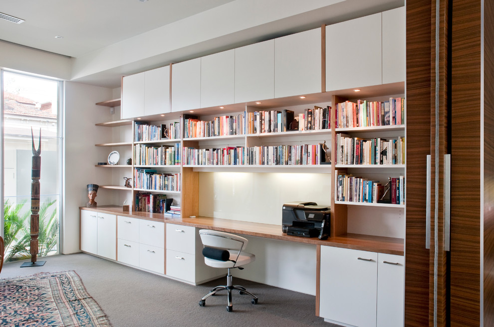 Inredning av ett modernt stort hemmabibliotek, med vita väggar, heltäckningsmatta och ett inbyggt skrivbord
