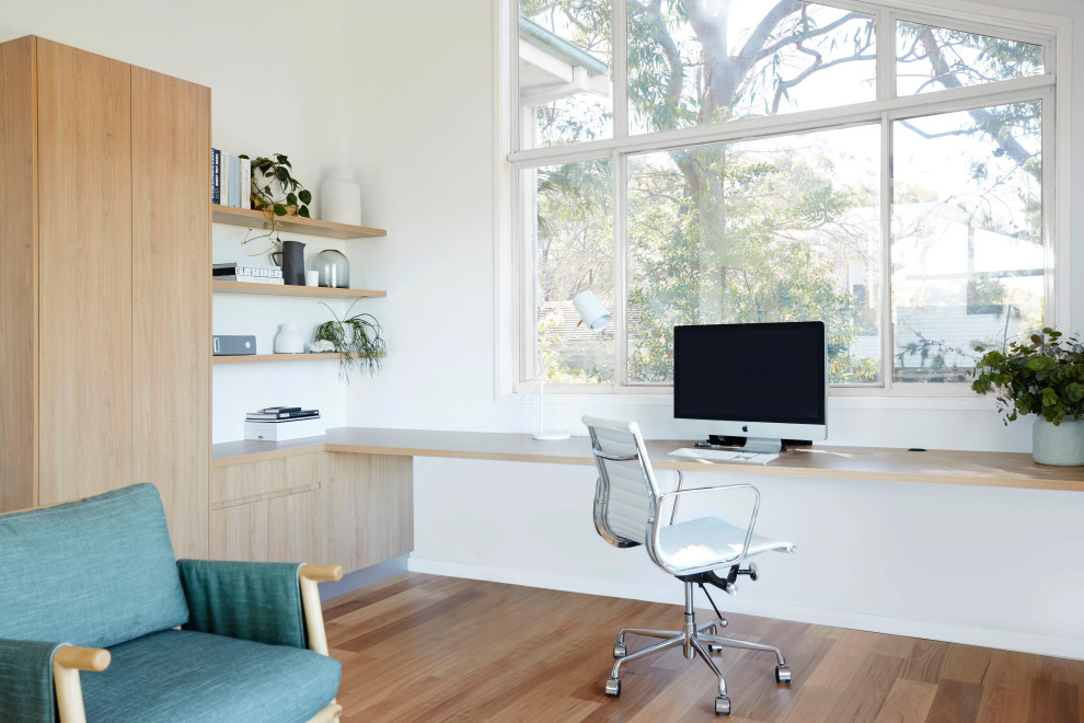 Bild på ett mellanstort funkis arbetsrum, med vita väggar, mellanmörkt trägolv, ett inbyggt skrivbord och brunt golv