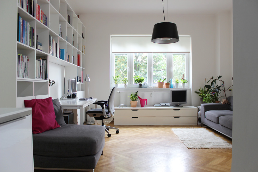 Modelo de despacho actual con paredes blancas, suelo de madera en tonos medios, escritorio independiente y suelo beige