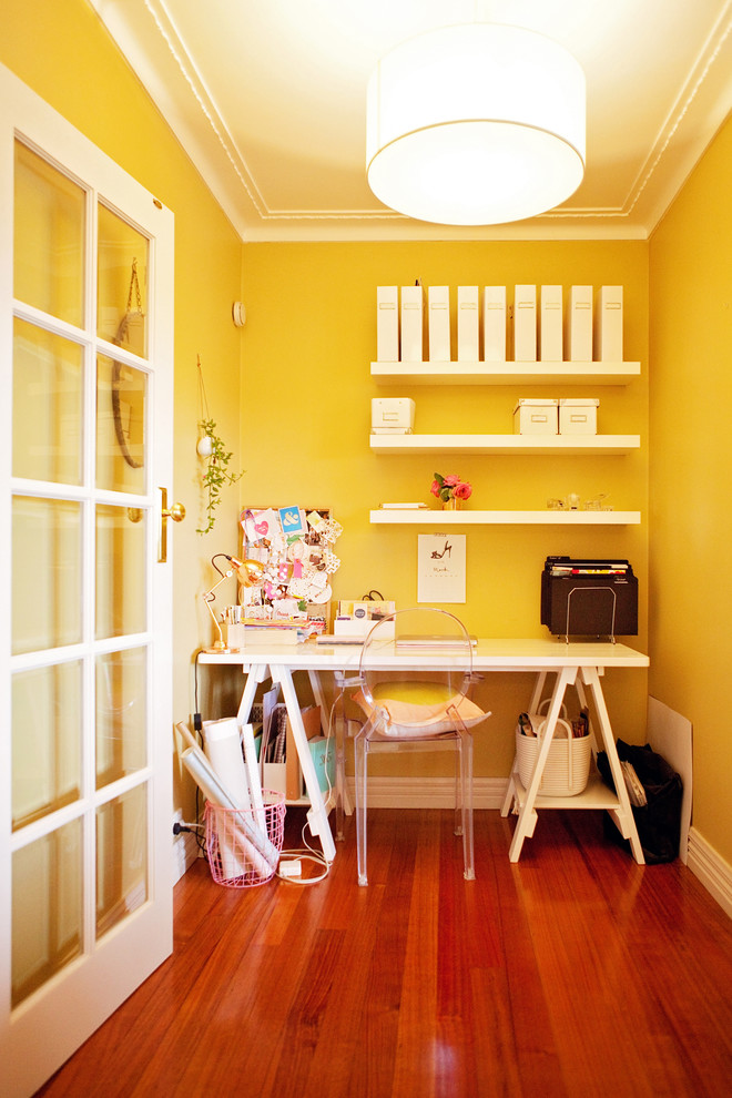 This is an example of a small contemporary home office in Melbourne with yellow walls, medium hardwood flooring, no fireplace and a freestanding desk.