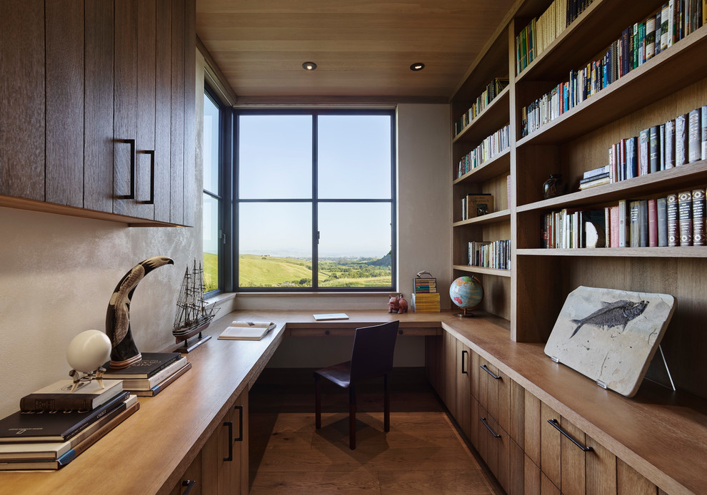 Réalisation d'un bureau chalet avec un sol en bois brun, une bibliothèque ou un coin lecture, un mur blanc et un bureau intégré.