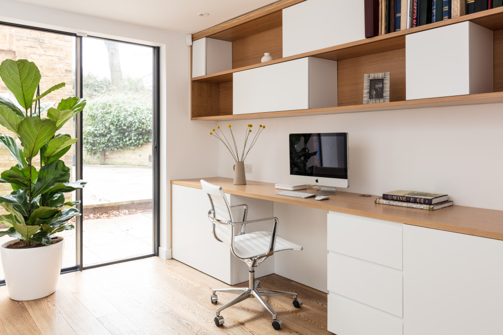Mittelgroßes Skandinavisches Arbeitszimmer ohne Kamin mit weißer Wandfarbe, hellem Holzboden, Einbau-Schreibtisch, Arbeitsplatz und beigem Boden in London