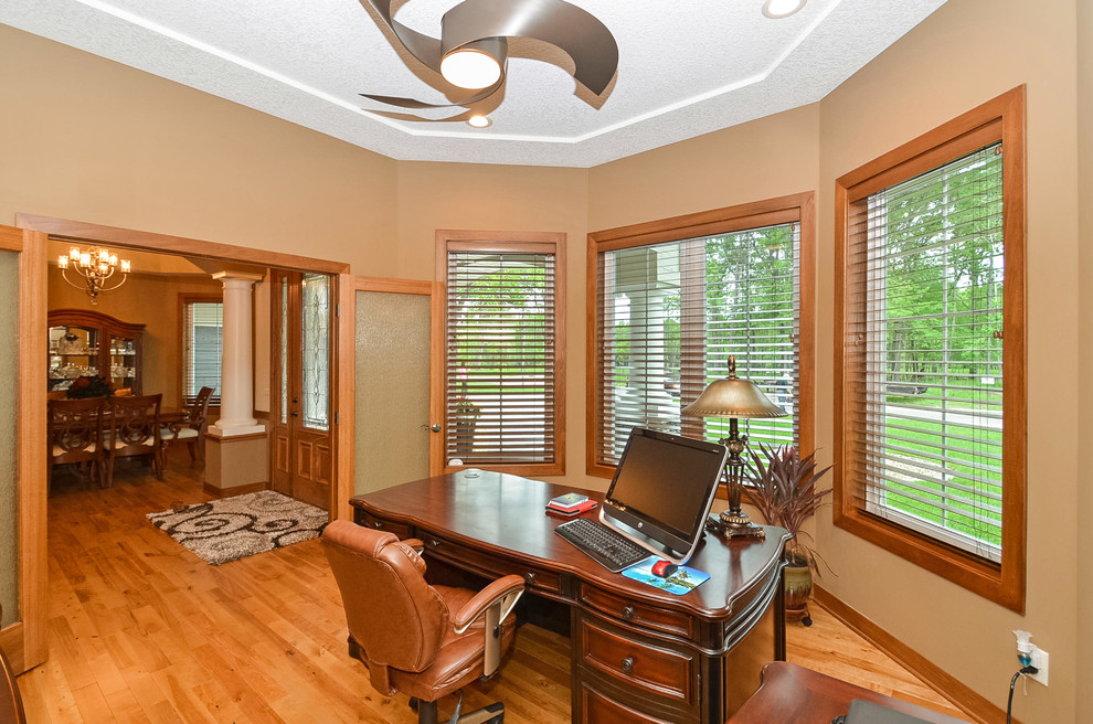 Diseño de despacho de estilo americano de tamaño medio sin chimenea con paredes beige, suelo de madera clara y escritorio independiente