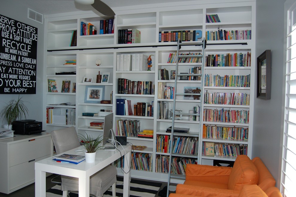 Lantlig inredning av ett mellanstort arbetsrum, med ett bibliotek, grå väggar och ett fristående skrivbord