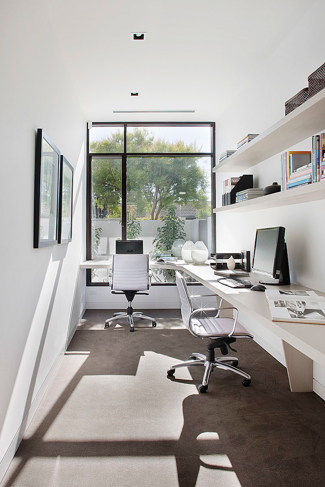 Foto på ett funkis hemmabibliotek, med vita väggar, betonggolv och ett inbyggt skrivbord