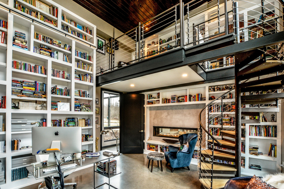 Cette photo montre un très grand bureau moderne avec une bibliothèque ou un coin lecture, un mur gris, sol en béton ciré, une cheminée double-face, un manteau de cheminée en béton et un bureau indépendant.