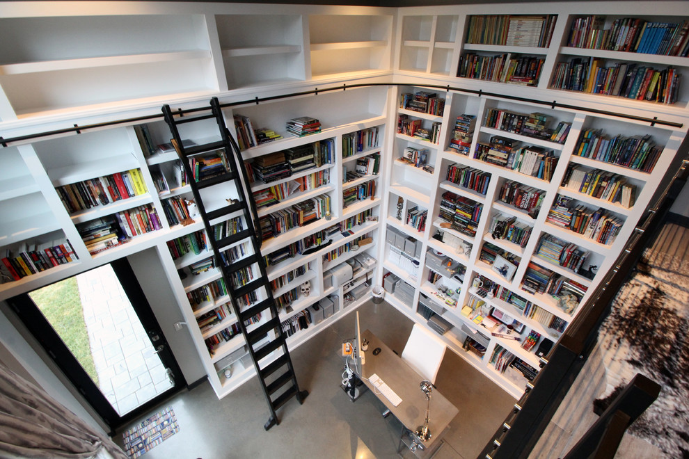 Exempel på ett stort modernt arbetsrum, med ett bibliotek, vita väggar, betonggolv, en dubbelsidig öppen spis, en spiselkrans i trä och ett fristående skrivbord