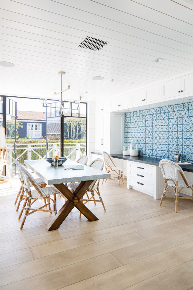 Imagen de sala de manualidades costera extra grande con paredes blancas, suelo de madera clara, escritorio empotrado y suelo beige