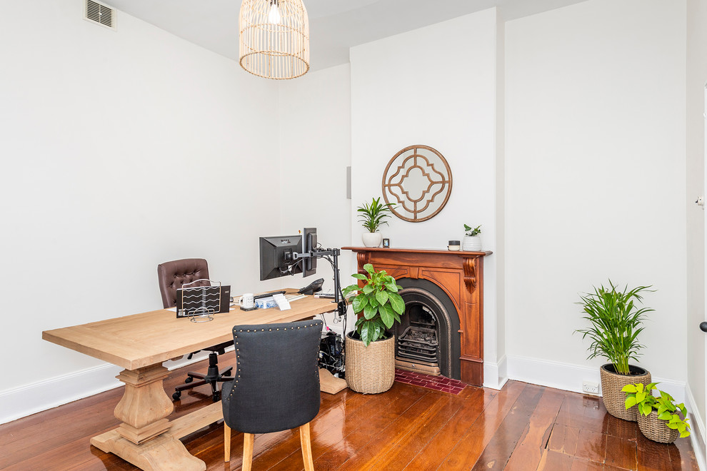 Imagen de despacho tradicional de tamaño medio con paredes blancas, suelo de madera oscura, todas las chimeneas, marco de chimenea de madera, escritorio independiente y suelo marrón