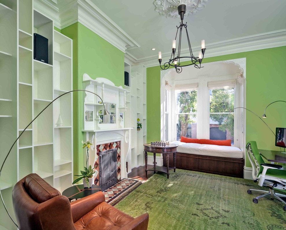 Klassisches Arbeitszimmer mit grüner Wandfarbe, dunklem Holzboden, gefliester Kaminumrandung, freistehendem Schreibtisch und grünem Boden in Los Angeles