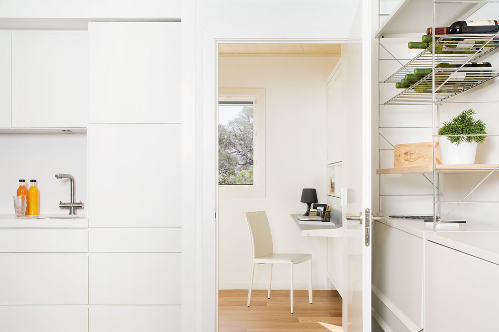Modelo de despacho contemporáneo pequeño sin chimenea con escritorio empotrado, paredes blancas y suelo de madera clara