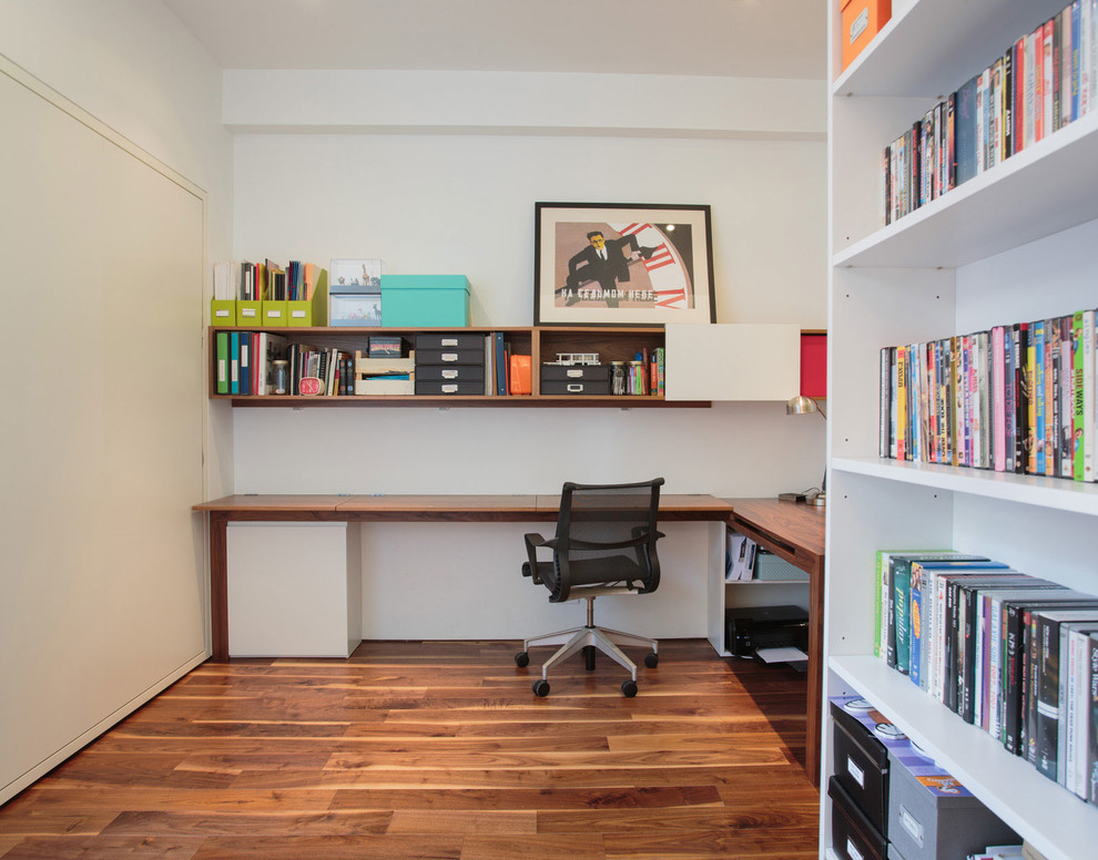 Kleines Modernes Arbeitszimmer ohne Kamin mit weißer Wandfarbe, braunem Holzboden, Einbau-Schreibtisch, Arbeitsplatz und braunem Boden in New York