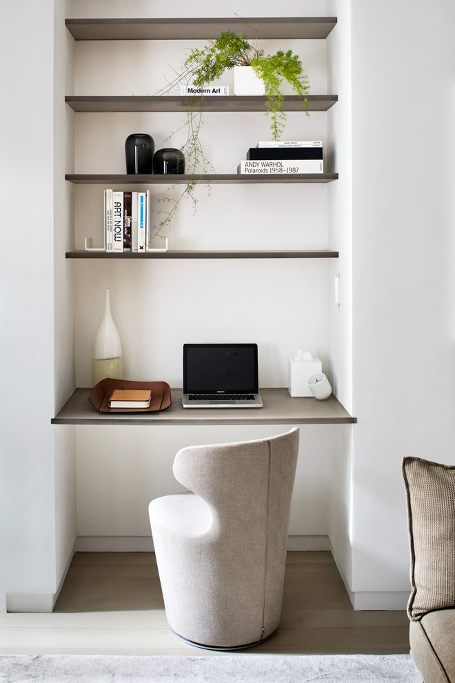 This is an example of a contemporary study in New York with white walls, light hardwood flooring and a built-in desk.