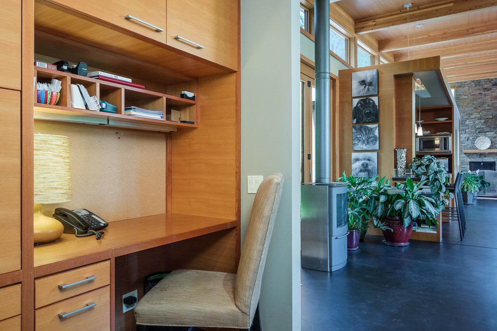 This is an example of a medium sized modern home office in Seattle with green walls, concrete flooring, a metal fireplace surround and a built-in desk.