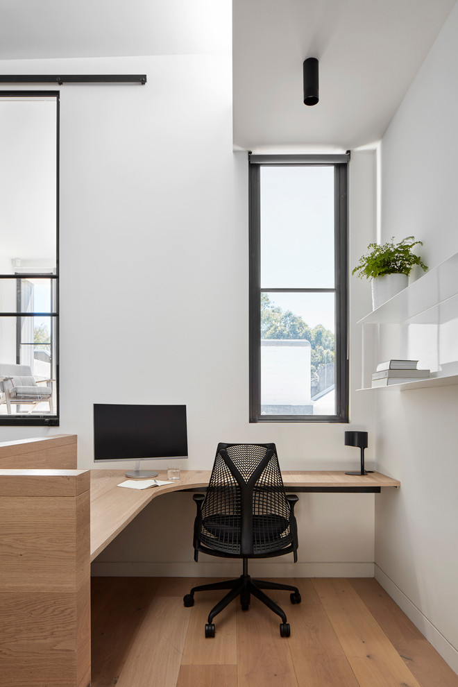 Foto de despacho actual con paredes blancas, suelo de madera clara, escritorio empotrado y suelo beige