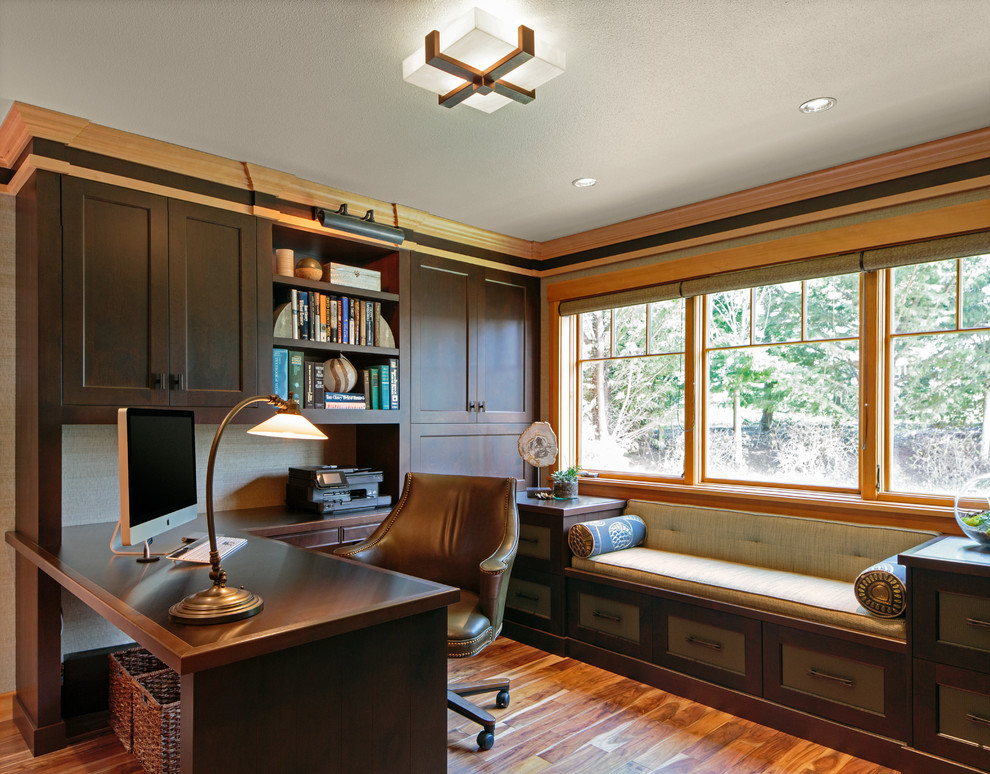 Foto på ett mellanstort funkis hemmabibliotek, med beige väggar, mellanmörkt trägolv och ett inbyggt skrivbord