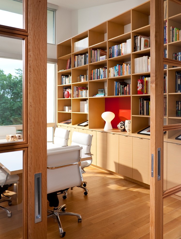 Bild på ett stort funkis hemmabibliotek, med vita väggar, ljust trägolv och ett fristående skrivbord