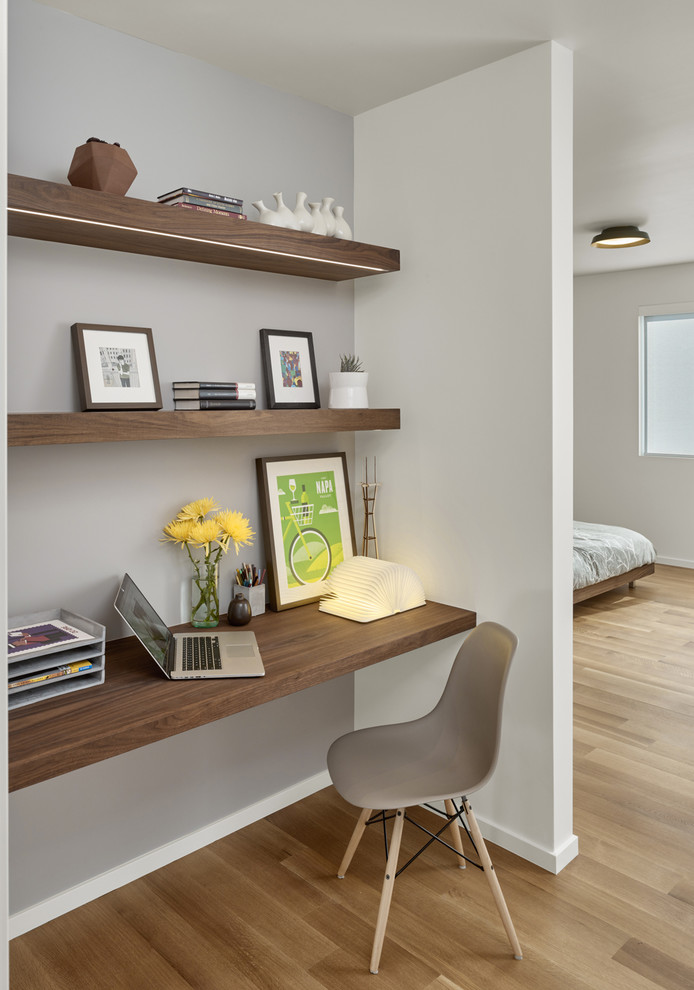 Diseño de despacho retro pequeño con paredes blancas, suelo de madera clara y escritorio empotrado