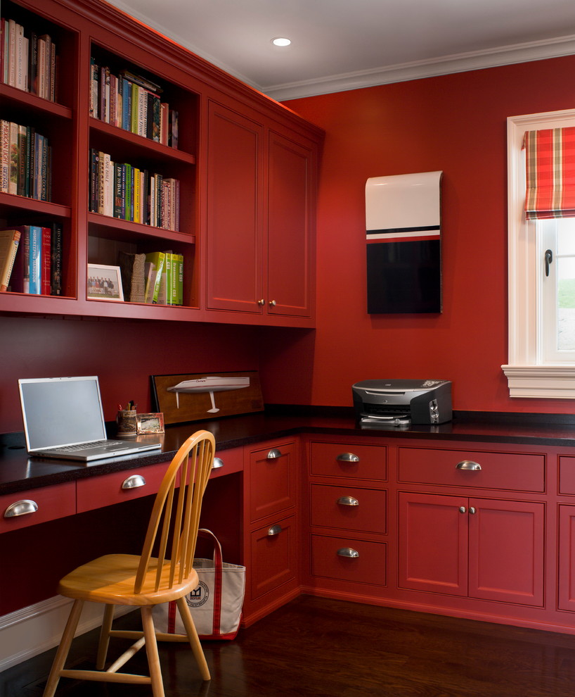 Diseño de despacho clásico renovado con paredes rojas, escritorio empotrado y suelo de madera oscura