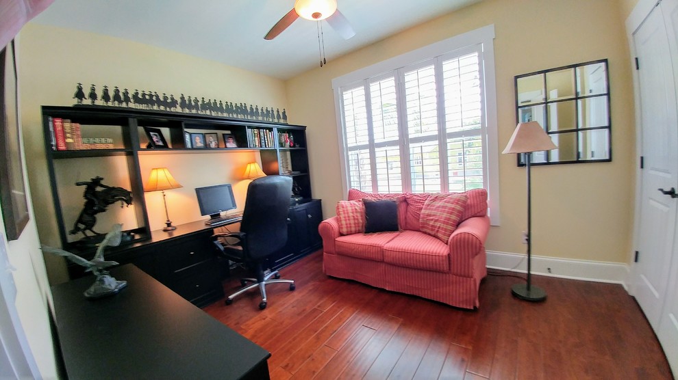 Ejemplo de despacho de estilo americano de tamaño medio con paredes amarillas y suelo de madera en tonos medios