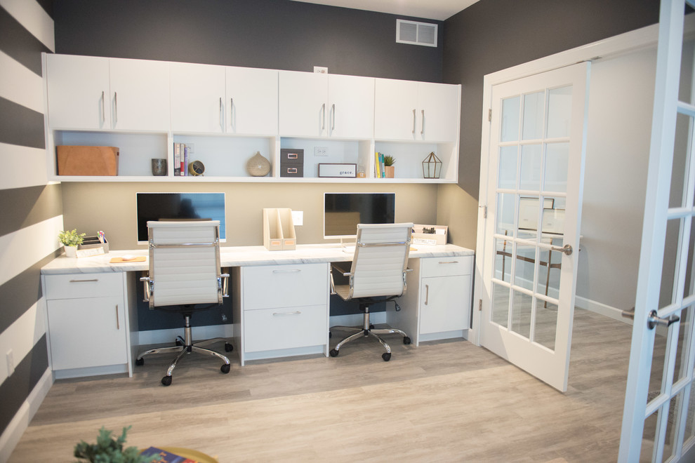 Imagen de despacho moderno grande con paredes grises, suelo laminado, escritorio empotrado y suelo gris
