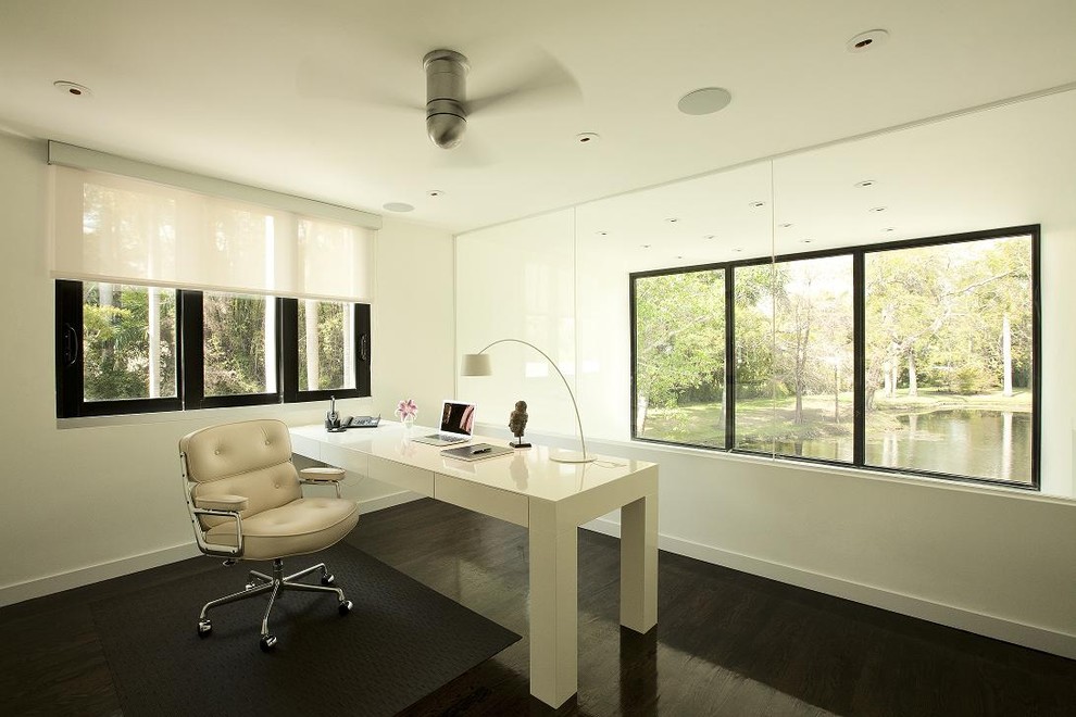Ejemplo de despacho actual con paredes blancas, suelo de madera oscura y escritorio empotrado
