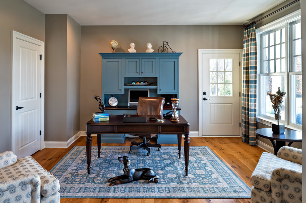 Imagen de despacho clásico con paredes grises, suelo de madera en tonos medios y escritorio independiente