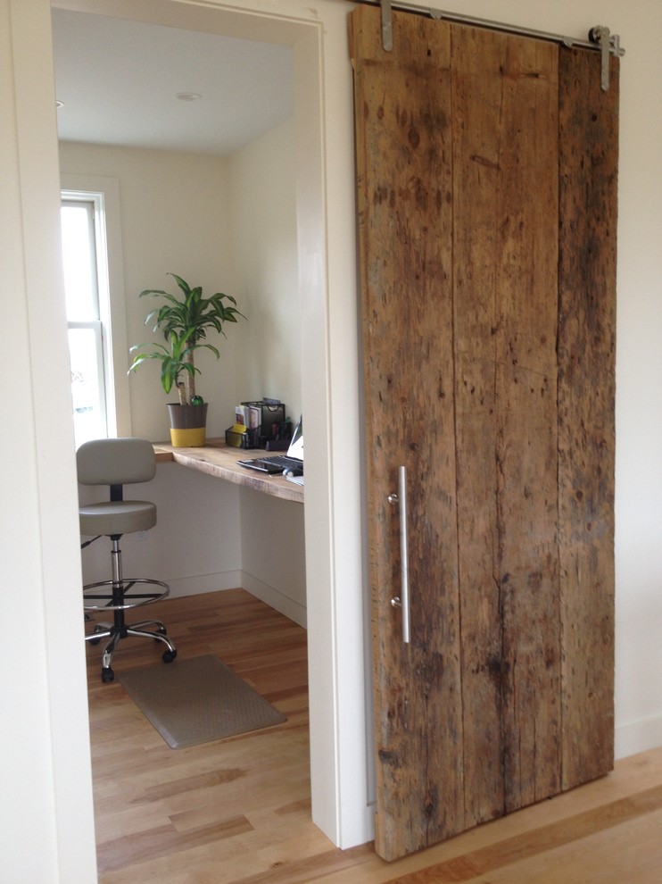 Modelo de despacho clásico renovado pequeño sin chimenea con suelo de madera clara, escritorio empotrado y paredes blancas