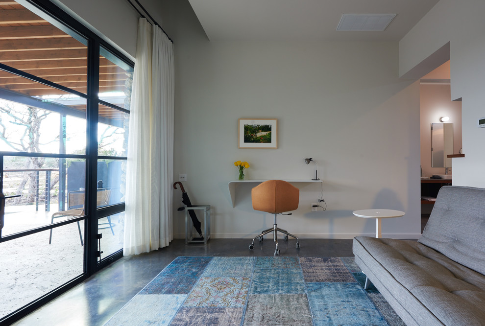Mittelgroßes Modernes Arbeitszimmer ohne Kamin mit weißer Wandfarbe, Betonboden, Einbau-Schreibtisch und grauem Boden in Austin
