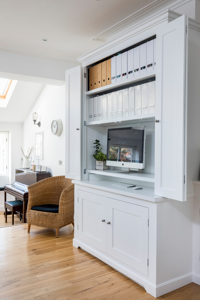 Diseño de despacho clásico pequeño con paredes blancas, suelo de madera clara, escritorio empotrado y suelo beige