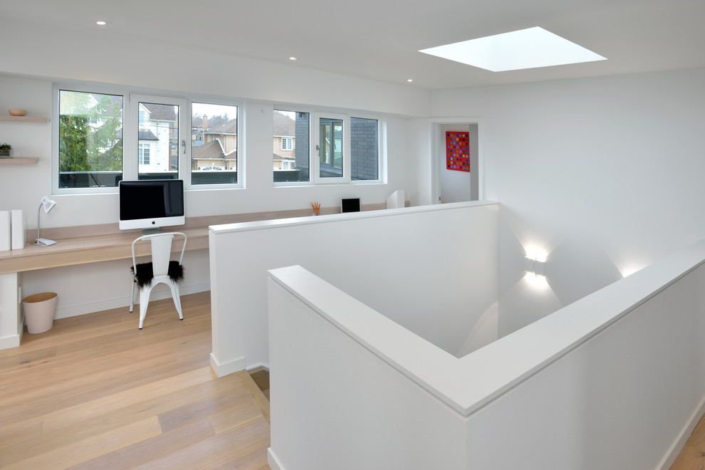 Ejemplo de despacho actual de tamaño medio con paredes blancas, suelo de madera clara, escritorio empotrado y suelo beige
