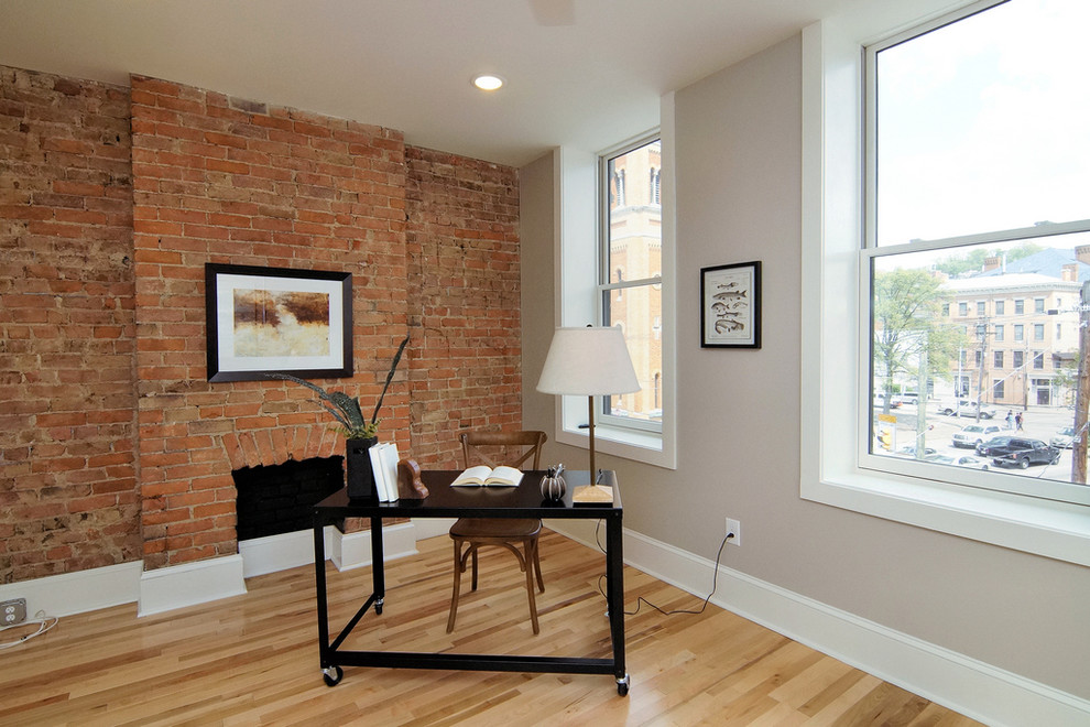Cette image montre un grand bureau urbain avec un mur gris, parquet clair, un bureau indépendant, une cheminée standard, un manteau de cheminée en brique et un sol beige.