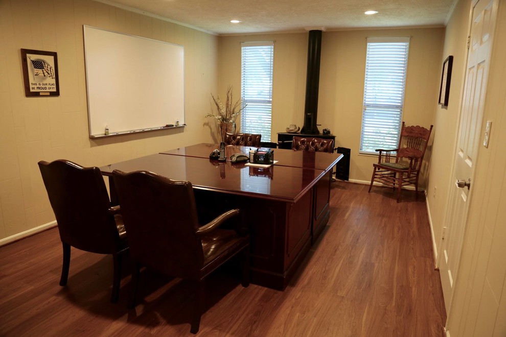 Cette image montre un grand bureau traditionnel avec un mur beige, un sol en bois brun, un poêle à bois, un bureau indépendant et un sol marron.