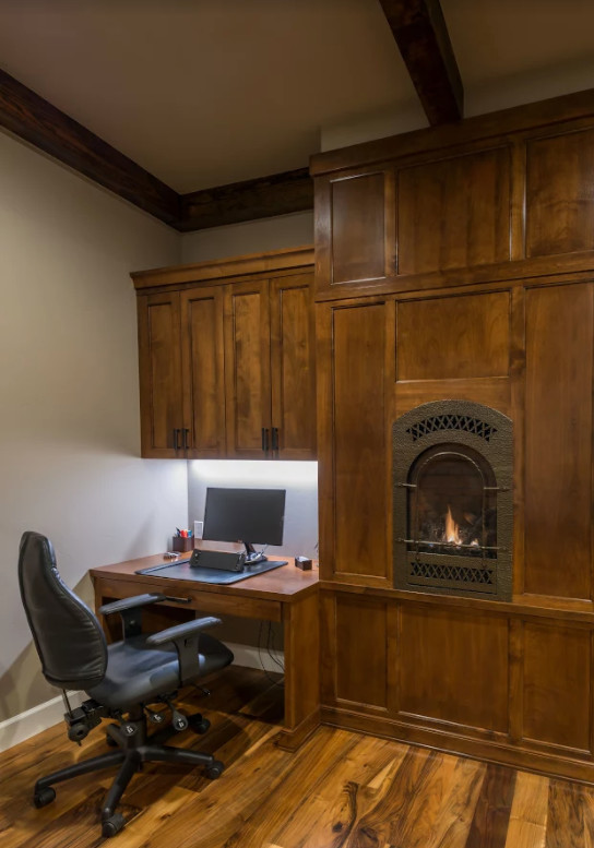 Esempio di un piccolo ufficio stile rurale con pareti grigie, parquet scuro, stufa a legna, cornice del camino in metallo, scrivania incassata e pavimento marrone