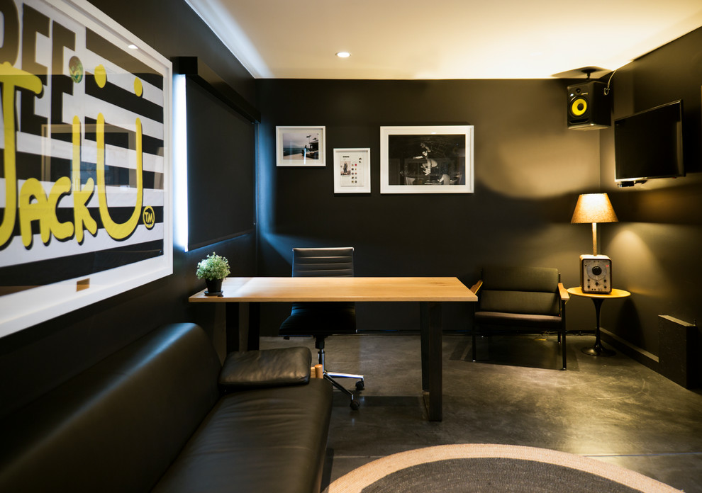 Mittelgroßes Eklektisches Arbeitszimmer mit Studio, schwarzer Wandfarbe, Betonboden, freistehendem Schreibtisch und schwarzem Boden in Los Angeles